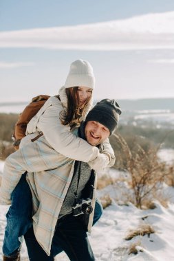 Baba, mutlu yetişkin kızını sırtında taşır, karlı bir kış gününde güler ve eğlenir.