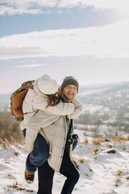 Mutlu baba kızını karlı bir dağ tepesinde sırtında gezdiriyor, kış tatilinin ve aile bağının tadını çıkarıyor.