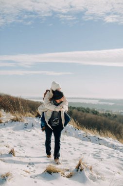 Baba, kızı karla kaplı bir tepede sırtında taşıyor. Kış günü eğlencesini ve sevgisini paylaşıyor.