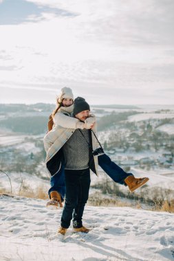 Mutlu bir baba, gülen kızını sırtında taşır ve karlı bir dağ manzarasında kışın eğlenir.