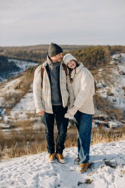 Baba ve kızı gülümsüyor ve el ele tutuşuyorlar, karlı bir dağda duruyorlar, birlikte mutlu bir kış anını paylaşıyorlar.