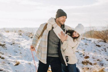 Baba ve kız kucaklaşıyorlar, gülümsüyorlar, karlı bir kış gününde dışarıda birlikte eğleniyorlar.