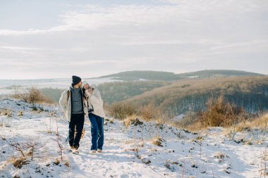 Baba, karlı bir tepede yürürken kızının başını öpüyor. Kış tatilinde hassas bir anı paylaşıyor.