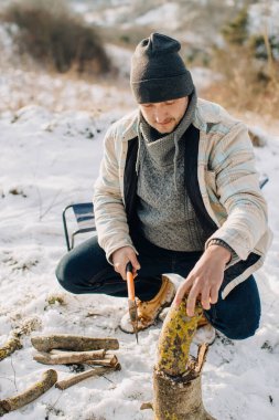 Soğuk bir kış gününde baltayla odun kıran bir adam. Doğada sıcak bir doğa deneyimi için hazırlanıyor.
