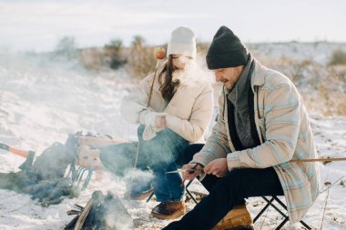 Baba ve kızı, karlı bir kış manzarasında, sıcak bir kamp ateşinde yemek pişiriyor, dışarıda kaliteli bir aile zamanı geçiriyorlar.