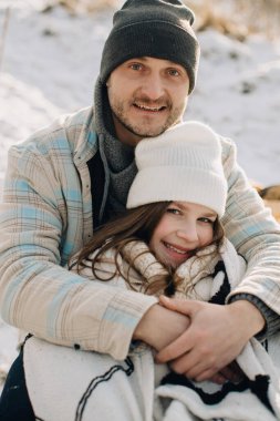 Gülümseyen baba kışın küçük kızını kucaklıyor, aile sevgisini ve birlikteliğini paylaşıyor.