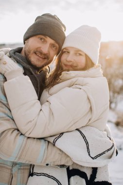 Baba ve kızı güneşli bir kış gününde açık havada sıcak bir kucaklaşmayı paylaşıyor, aile bağlarını ve sevgiyi yansıtıyor.
