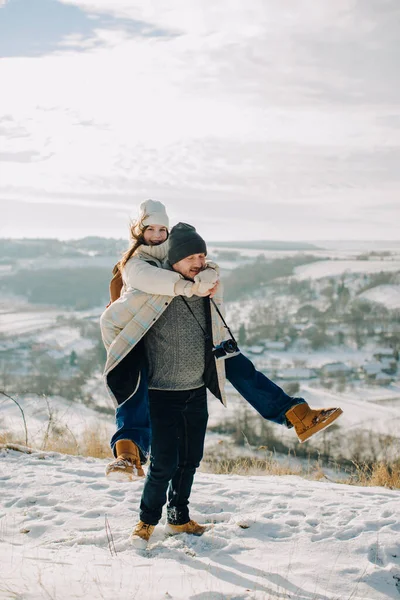 Mutlu bir baba, gülen kızını sırtında taşır ve karlı bir dağ manzarasında kışın eğlenir.