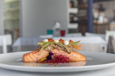 Krem soslu tavada kurutulmuş somon filetosu ve restoran ortamında servis edilen taze sebzeler. Zarif sunum ve güzel yemek konsepti..