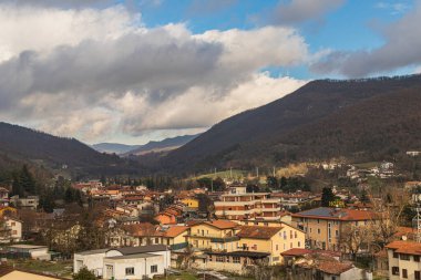 Dağ manzarasıyla çevrili yerleşim binaları ve oteli olan İtalyan kasabası manzarası. Barışçıl Avrupa ortamında taşra mimarisi ve bulutlu gökyüzü.