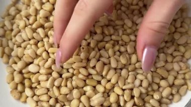 Beyaz arka planda çam fıstığı. Manikürlü bir kadın onlara dokunduğunda vitamin dolu doğal sağlıklı yiyecekler ve beslenme dengesi ve temiz yeme konsepti için mükemmel enerji gösterir..