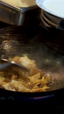 Çelik bir tavada lezzetli yumurtalı burji masala yapan bir kadın, akşam yemeği için mutfak malzemelerini karıştırıp çırpıyor. Yüksek kalite 4k görüntü