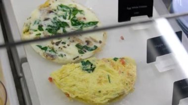 Lezzetli kahvaltı gösterisi kızarmış yumurta, taze sebzeler, ekmek ruloları ve ahşap bir masada ustalıkla hazırlanmış baharatlar içerir. Sağlıklı yemek temaları için ideal. Yüksek kalite 4k görüntü