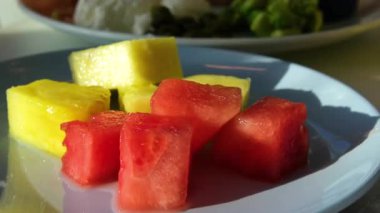 Yıldız meyvesi, mango, ananas, karpuz ve ananas parçalarından oluşan çeşitli meyve parçaları güneş ışığı kırmızı meyveleriyle yıkanmış gri bir tabakta.