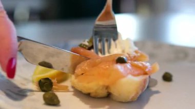 Pişmiş somon ve krem peynirli simit, masa bıçağı ve çatalla yenmeye başlar. Yakın çekim. Kahvaltıda popüler yemek, iştah açıcı ve taze görünüyor. Yüksek kalite 4k görüntü