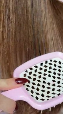 Kahverengi saçlı, pembe taraklı, dalgalı, parlak, dikey kadın saçı videosuyla tarayan bir kızın yakın çekimi. Yüksek kalite 4k görüntü