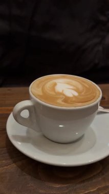 İnsanlar bir fincan kahveyi latte sanatıyla birlikte tutuyorlar. Sabah kahve konsepti. Bir kupa sıcak kahve ve buğulanmış sütle doldurulur, üstü de latte sanatıyla kaplanır. Yüksek kalite 4k görüntü