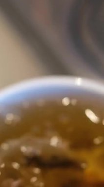 Çay yaprakları ve taze limon dilimleri şeffaf bardakta sıcak suyla döner. Ahşap masada cam bardakta bitki içeceği demleme işlemi. Yüksek kalite 4k görüntü