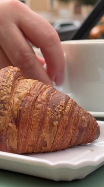 Sabah kahvaltısı kızı, sokak yabancılarının yanında Avrupa kruvasanı yiyen bir kafede bir fincan cappuccino içiyor. Yüksek kalite 4k görüntü
