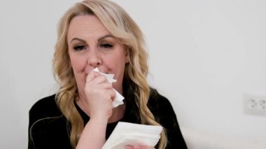 Hapşıran beyaz kadın hapşırıyor ve evdeki dokulara burnunu siliyor. Yüksek kalite 4k görüntü