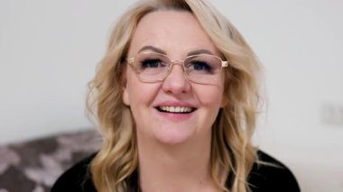 Gözlüklü yetişkin bir kadın gülüyor. Doğrudan kameraya bakıyor. Onaylanan mutluluk ve olumlu duyguyu yansıtıyor..