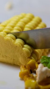 Gerçekçi mısır şekilli ezme beyaz bir tabakta özgün moleküler gastronomi yemek sunumunda kremsi doku sanatsal ve yenilikçi mutfak tasarımı ile servis edilir..