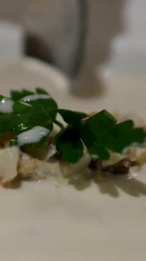 Yumuşak bir kaptan servis edilen kremalı midye çorbası tabağın üzerine dökülüyor. Zarif sunum zengin ve lezzetli yemek deneyimi modern mutfak sanatları..