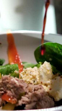 Restoranda beyaz tabakta duran kızarmış ton balığı, yumurta, domates ve salata yapraklarının üzerine soya sosu dök. Yavaş çekim el kamerası videosu. Deniz ürünleri teması. Yüksek kalite 4k görüntü