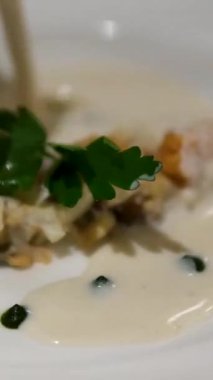 Yumuşak bir kaptan servis edilen kremalı midye çorbası tabağın üzerine dökülüyor. Zarif sunum zengin ve lezzetli yemek deneyimi modern mutfak sanatları..