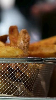 Kırmızı ekose masa örtüsü üzerinde metal bir sepetin içinde çıtır çıtır patates kızartması. Günlük yemek, fast food ya da Amerikan mutfağı için mükemmel. Arka planda bir adam bir bardak kola getiriyor.