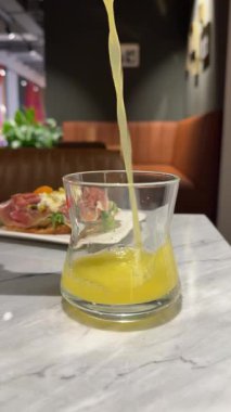 Taze portakal suyu bardağa dökülüyor güneşli ahşap mutfak masasında ve gri duvar arkasında, ağır çekimde. Yüksek kalite 4k görüntü