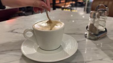 Adamın eli kahveyi fincanda karıştırır, kahve fincanını tuğladan sırtüstü çevirir, latte sanat kahvesini karıştırmak için kaşığı yavaşça tutar. Yüksek kalite 4k görüntü