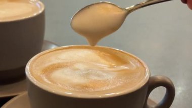 İçi sıcak kahve dolu, köpüklü, kalın bir kahve fincanı ve içinde kahve aşıkları için mükemmel bir kaşık olan bir kaşık. Yüksek kalite 4k görüntü