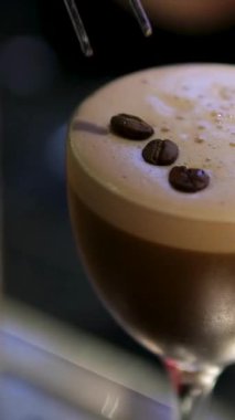 Bir el kırsal ahşap bir masada espresso martinisine uzanır, kremalı dokuya ve kahve çekirdeklerine vurgu yapar. Yüksek kalite 4k görüntü