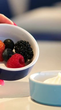 Ahududu ve böğürtlenli Yunan yoğurdu, bir kâseden kaşıkla kepçelenmiş, yakın plan, üst manzara. Taze ahududu ve ardından Yoğurda Düşen Kamera.