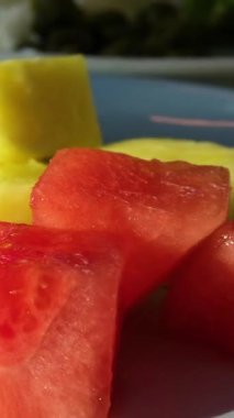 Yıldız meyvesi, mango, ananas, karpuz ve ananas parçalarından oluşan çeşitli meyve parçaları güneş ışığı kırmızı meyveleriyle yıkanmış gri bir tabakta.