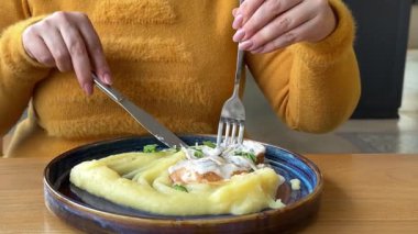 Restoranda patates püresi ve kremalı soslu kafede et yiyen bir kadın. Sarı ceketli bir öğle yemeğinde. Yüksek kalite 4k görüntü