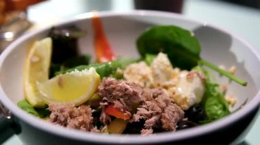 Konserve ton balıklı salata, domates, fıstık, mango, avokado, kereviz, acı biber ve siyah susam. Zeytinyağlı yaz salatası ve limon lobu. Kadın domates ekliyor. Seçici.