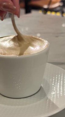 Adamın eli kahveyi fincanda karıştırır, kahve fincanını tuğladan sırtüstü çevirir, latte sanat kahvesini karıştırmak için kaşığı yavaşça tutar. Yüksek kalite 4k görüntü