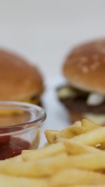 Yakın plan çekimde, çıtır çıtır bir patates kızartmasını klasik bir peynirli burger ve arka planda patates kızartmasıyla zengin bir ketçap ya da sosa batırıyorum. Yüksek kalite 4k görüntü