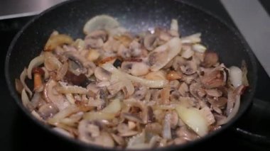 Fırının tepesinde kızartma yaparken doğranmış soğan ile dilimlenmiş düğme mantarlarının tuzlanması. Kızartma tavasındaki tuzlu mantarlar