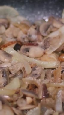 Fırının tepesinde kızartma yaparken doğranmış soğan ile dilimlenmiş düğme mantarlarının tuzlanması. Kızartma tavasındaki tuzlu mantarlar