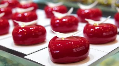 Parlak kırmızı kalp şeklinde tatlı, beyaz çikolata tüyü ve altın yaprağıyla süslenmiş, zarif siyah çatal bıçak takımının yanında duran, romantik ve lüks. Yüksek kalite 4k görüntü