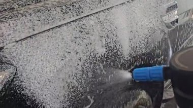 Yeni siyah, su ve köpükle yıkanacak, büyük modern araba dış temizliği, oto yıkamada parlak araç, görünür markası veya logosu olmayan jenerik otomobil.