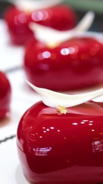 Parlak kırmızı kalp şeklinde tatlı, beyaz çikolata tüyü ve altın yaprağıyla süslenmiş, zarif siyah çatal bıçak takımının yanında duran, romantik ve lüks. Yüksek kalite 4k görüntü