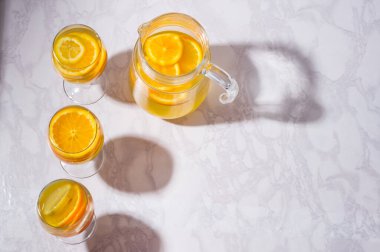 Portakal, limon ve greyfurtlu limonata sürahisi. Beyaz masadaki yukarıdan bir bardak limonata..