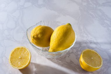 Dilimlenmiş ve bütün limonlar beyaz bir masada ve cam bir kasede. C vitamini konsepti. Beyaz arkaplan
