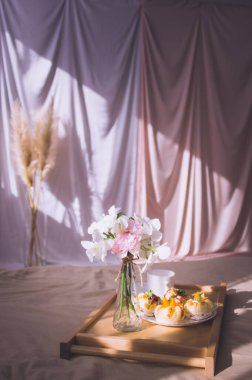 Kahveyle, çörekle, oteldeki ya da evdeki ahşap tepside çiçeklerle yatakta kahvaltı. Pencere ışığı