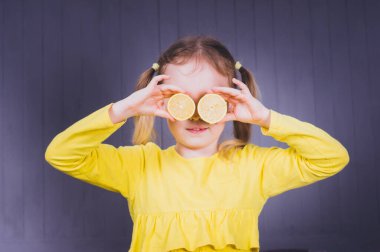 Gri ahşap arka planda gözlerinde taze limon tutan küçük tatlı bir kız çocuğu.