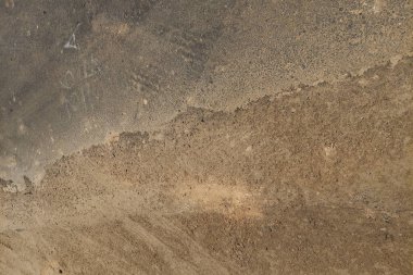 Kum ve asfalt bir yüzey. Havalandırma ve malzeme aşınmasından kaynaklanan görünür doku değişimleri var..